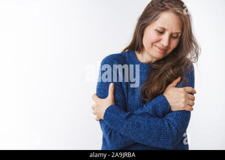 La tendresse et la notion de famille. Doux et tendre belle femme d'âge moyen en sweater hugging elle-même avec les mains croisées sur le bras à la timide et c Banque D'Images