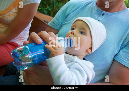 Un petit enfant est assis et des boissons de l'eau d'une bouteille. Banque D'Images