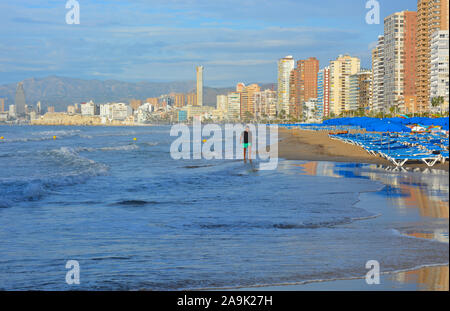 Benidorm ville et plage de Playa Levante, tôt le matin avec l'homme de marcher sur la plage et des réflexions dans le sable humide Banque D'Images