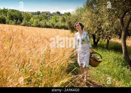 Vêtements femme dans la quarantaine, promenades dans la campagne italienne, à côté d'un champ de blé, transportant un panier de cerises Banque D'Images