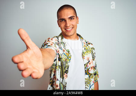 Jeune homme séduisant en vacances portant chemise hawaïenne sur fond blanc smiling friendly offrant comme message d'handshake et accueillant. Succès Banque D'Images