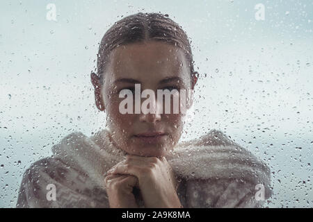 Portrait d'une femme triste à la recherche de l'extérieur dans la maison par une fenêtre couverte de gouttes, portrait authentique d'une fille calme Banque D'Images