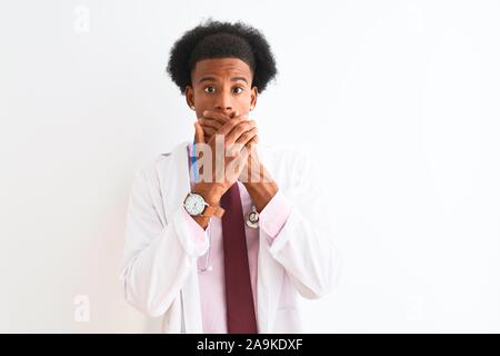 Young african american man wearing sthetoscope médecin isolé sur fond blanc choqué couvrant la bouche avec les mains pour l'erreur. Concept Secret. Banque D'Images