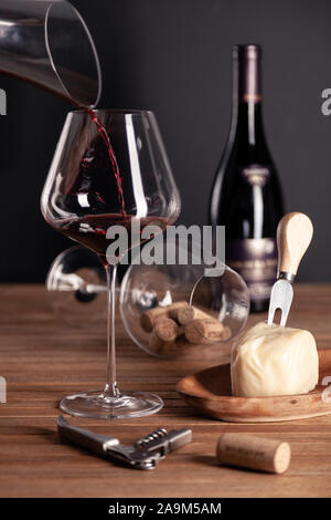 Verser le vin rouge dans le verre cristal, bouteille, tire-bouchon, ouvre-boîte, couteau sommelier, décanteur transparent, bouchons, du fromage sur la table en bois. Gros plan, vertical, Banque D'Images