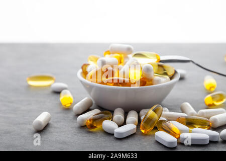 Médecine dispersés vitamines, pilules, médicaments au bol avec cuillère en métal sur fond gris. Complément alimentaire aliments blancs écossés dur rempli de capsules Banque D'Images