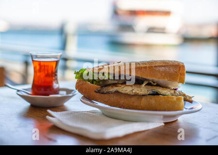 Sandwich de poisson d'Istanbul. Burger avec du poisson frit. Du thé turc avec Balik Ekmek. Arrière-plan flou avec vue sur la mer Banque D'Images