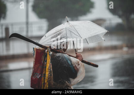 Sapa, Vietnam - 13 octobre 2019 : Un vieux homme asiatique sous un parapluie s'éloigne de la caméra dans la pluie battante dans la petite ville de Sapa Banque D'Images