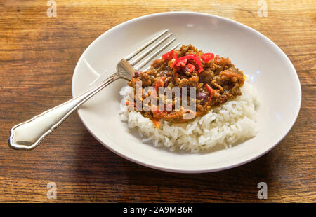 Un bol blanc de fraîchement cuit accueil chili con carne et riz avec une fourchette garnie de piment rouge haché et placés sur une planche en bois Banque D'Images