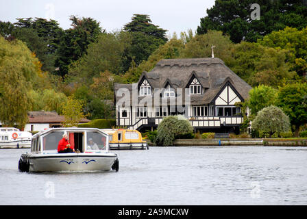 Belle maison au toit de chaume à côté de la rivière Bure, Norfolk, Angleterre, avec des bateaux sur la rivière Banque D'Images