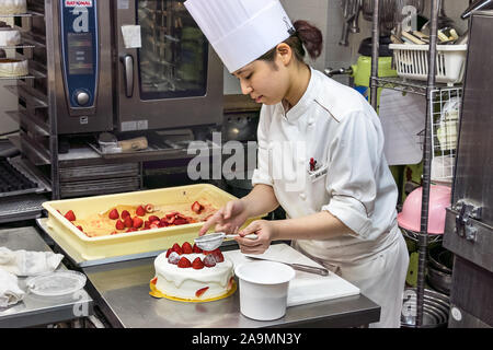Une femme japonaise pastry chef decorating un gâteau avec du sucre en poudre. Banque D'Images