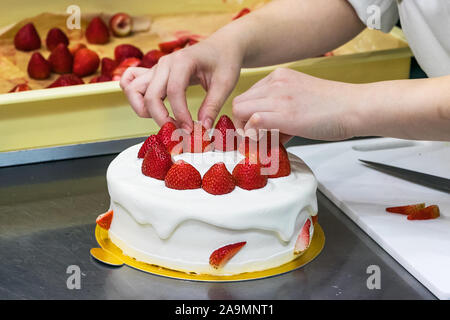 Chef pâtissier femelle mains, Décorer un gâteau à la crème avec les fraises. Banque D'Images