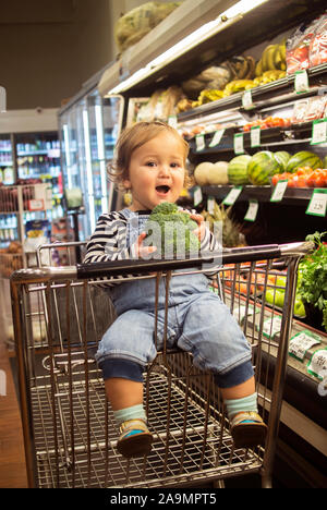 A smiling baby takes something le brocoli dans la production d'un marché de l'isle Banque D'Images