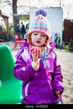 Cute little girl dans des vêtements d'hiver de groseille rouge ses études sereinement la crème glacée la crème glacée en hiver - concept Banque D'Images