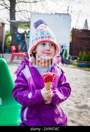 Cute little girl rend drôle de visage savourant sa glace fruits rouges sur une journée d'hiver Banque D'Images