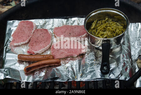 Côtelettes de porc grillées et des hot-dogs avec haricots verts au-dessus de feu de camp. Détente et de préparer les aliments à l'extérieur. La détente et les loisirs. Banque D'Images