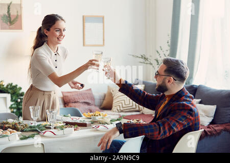 Portrait de belle jeune femme clinking glasses avec mari dans votre salle à manger élégante table set pour célébrer Noël, copy space Banque D'Images