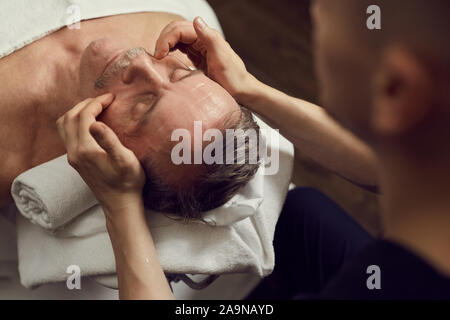 High angle portrait of handsome man enjoying massage du visage au centre de spa de luxe, copy space Banque D'Images