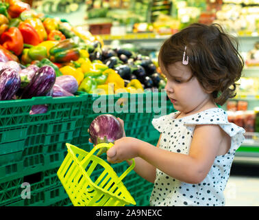 Shopping enfant aubergines dans un supermarché. Concept pour l'achat de fruits et légumes dans les hypermarchés. Petite fille tenir panier. Banque D'Images