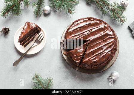 Gâteau de Noël au chocolat sur fond gris clair, vue du dessus, copiez l'espace. Gâteau au chocolat classique avec le chocolat noir et branches de sapin de Noël. Banque D'Images