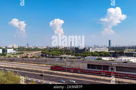 Trois nuages au-dessus de la thunder nord de Tel aviv skyline avec luna park, l'autoroute ayalon, et un train à l'avant-plan Banque D'Images