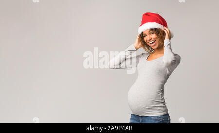 Femme enceinte excité à Santa hat posing sur fond gris Banque D'Images