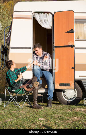 Femme assise sur chaise de camping et en regardant son petit ami assis sur l'escalier de leur Retro camping-van. Banque D'Images