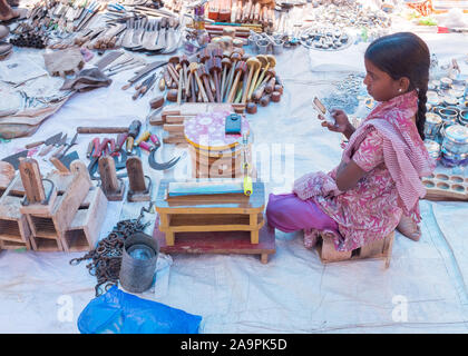 Jeune fille assise à son étal jouer avec téléphone mobile au marché du dimanche de l'Inde, Tiruchirappalli Banque D'Images