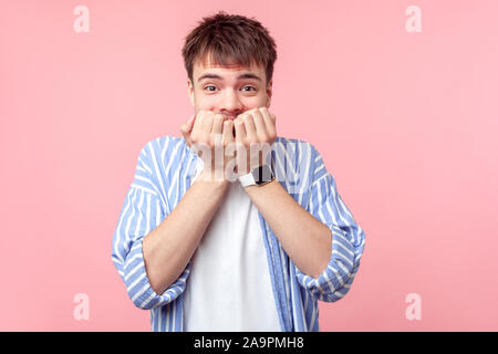 Portrait de Coward, peur nerveux brown-haired man in casual chemise rayée mordre ongles, looking at camera avec peur terrifié expressio Banque D'Images
