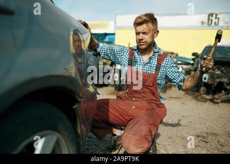 Réparateur d'hommes travaille avec marteau sur location junkyard Banque D'Images