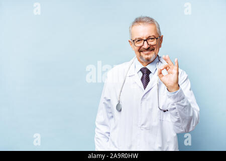 Young doctor posing and smiling at camera, santé et médecine. Isoler sur fond bleu. Médecin montre un ok Banque D'Images