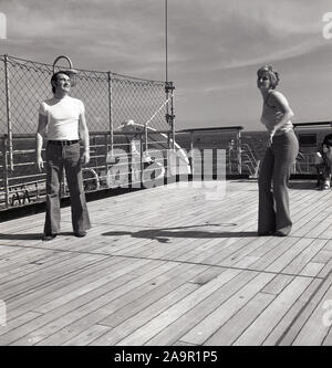 Fin des années 60, historique, deux passagers à bord d'un navire de croisière en dehors de la lecture d'un jeu de carte - avis leur flair pantalons, le goût du jour. Banque D'Images