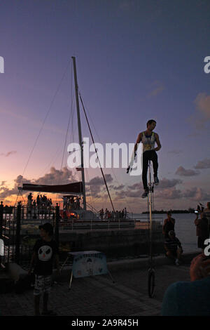 Un artiste de rue jonglant avec des bâtons de feu sur un unicycle à une foule à Mallory Square Key West Florida Banque D'Images