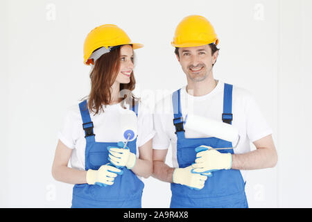 Deux peintres en uniforme de happy house holding rouleaux à peinture dans maison neuve. Réparation, construction et concept d'hypothèques. Banque D'Images