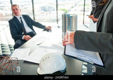 Réunion des architectes et investisseurs commerciaux, modèle de bâtiment résidentiel moderne de plusieurs étages maison de plans et casque sur la table , la construction de pla nification Banque D'Images