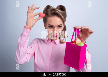 Funny blond woman holding gift bag de macarons colorés Banque D'Images