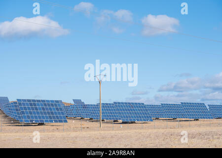 Panneaux solaires avec champ tracker pour la production d'énergie durable avec un mât électrique au premier plan pour le transport de l'électricité générée, Banque D'Images