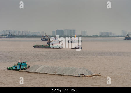 Tau Long River, au Vietnam - 12 mars 2019 : Petit bateau bleu pousse longue péniche remplie de pierres gris brun sur le fleuve. D'autres navires et des bâtiments o Banque D'Images