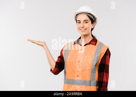 Pretty young female builder dans un casque de protection et des vêtements présentant quelque chose Banque D'Images