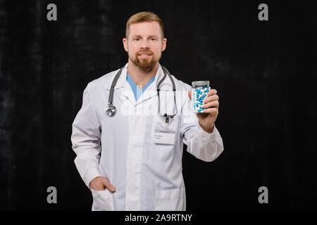 Jeune médecin barbu blanchon en tenant la bouteille de comprimés Banque D'Images