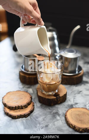 Faire le café glacé vietnamien. Femme svelte part verser du café noir en verre avec de la glace et le lait condensé sur fond sombre copy space Banque D'Images