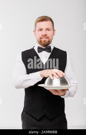 Jeune garçon élégant en noir et gilet bowtie holding cloche avec repas Banque D'Images