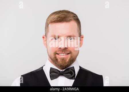 Young smiling waiter barbu en noir et gilet bowtie vous regarde Banque D'Images