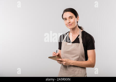 Jeune et jolie brunette serveuse dans des notes sur l'aire de l'ordre dans le bloc-notes Banque D'Images