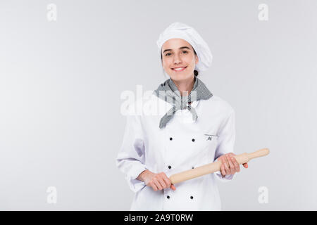 Pretty young smiling chef holding uniforme blanc dans l'axe de roulement pendant la cuisson Banque D'Images