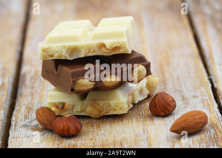 Morceaux de blanc et de chocolat au lait aux amandes et noisettes empilés sur la surface en bois Banque D'Images