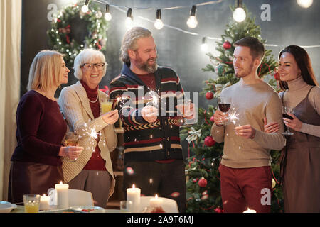 Cheerful adultes avec feux de Bengale mousseux chatting at Christmas party at home Banque D'Images