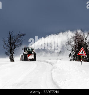 Un tracteur travaillant comme un chasse-neige découvre une route couverte de neige, la neige s'envole dans un ciel sombre, arc, signe pour les cyclistes - Emplacement : border reg Banque D'Images