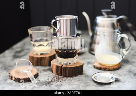 Verser sur la préparation du café vietnamien avec le lait condensé. L'écoulement du café dans un verre de NIMP sur fond sombre copy space Banque D'Images