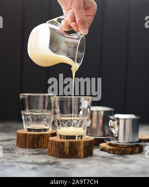 Verser sur la préparation du café vietnamien. Femme part verser dans des verres de lait condensé sur fond sombre copy space Banque D'Images