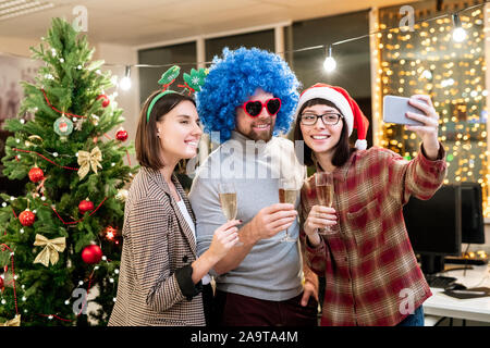 Trois jeunes travailleurs de bureau avec des flûtes de champagne à l'appareil photo de votre smartphone à Banque D'Images